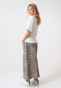 Top bianco arricciato abbinato a una lunga gonna leopardata. L'outfit presenta un orlo arricciato e sneakers bianche casual con dettagli viola.