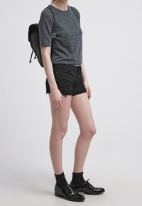 Šedé tričko s krátkým rukávem, černé džínové kraťasy s důlky, černé kotníkové ponožky, lesklé černé oxfordky a černý batoh.