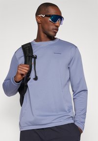 Ανοιχτό μωβ αθλητική μπλούζα με μακριά μανίκια και υφή, στρογγυλή λαιμόκοψη και μαύρη θήκη σακιδίου. Το μοντέλο φοράει υπερμεγέθη ανακλαστικά γυαλιά ηλίου.