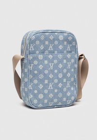Džínová crossbody taška vo svetlom modrom odtieni s bielymi monogramovými vzormi. Obsahuje zips a hnedý nastaviteľný popruh. Obdĺžnikový tvar.