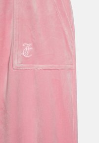 Ρόδινo βελούδινο ρούχο με μπροστινή τσέπη που έχει κεντημένο το γράμμα «F». Η υφή είναι απαλή και λείαινα, με μια ελαφριά γυαλάδα.