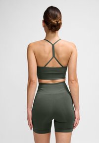 Olijfgroene sportoutfitset met een aansluitende sportbeha met spaghettibandjes en hoog getailleerde shorts. Glad textuur, minimalistisch ontwerp.