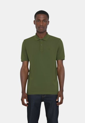 Polo verde realizzato in tessuto liscio, con un colletto, due bottoni, maniche corte e un design semplice, abbinato a jeans scuri.