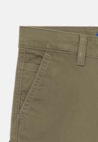 Khakifärgade byxor tillverkade av robust bomullsmaterial med blandning. Har en platt front, bältesslevar och två sidofickor med en slät yta.