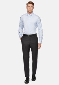 Světle modrá košile s dlouhým rukávem a špičatým límečkem, kombinovaná s černými kalhotami na míru a černými šněrovacími botami, s elegantním designem.