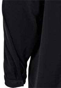 Blouse noire avec des manches longues amples. Tissu doux avec une texture lisse. Présente une manche à poignet avec un détail de bouton.