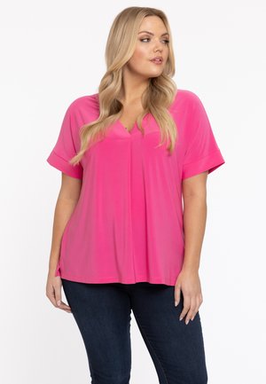 Korte mouwen, V-hals top in een levendige roze stof, met een losse pasvorm, zijsplitten en een gladde textuur. Gecombineerd met donkere jeans.