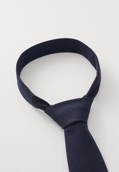 Cravatta di seta blu navy con un motivo a spina di pesce solido, caratterizzata da una texture liscia e un design annodato al centro.