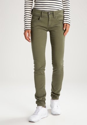 Jean slim fit vert olive avec une texture lisse et un design à cinq poches, présentant une fermeture boutonnée et porté avec des baskets blanches.