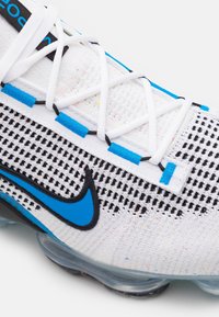 Nike Air VaporMax med ett vitt nätövre, svarta och blå accenter, synligt snörningssystem och en dämpad transparent sula.