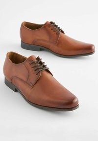 Chaussures à lacets en cuir brun avec une texture lisse, bout arrondi et détails de couture simples. Semelle en caoutchouc noir pour la durabilité.