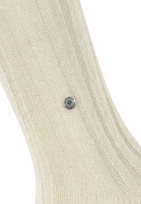 Calzino a maglia color crema con texture a coste e un bottone metallico rotondo con marchio inciso sul lato.