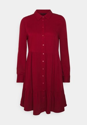 Červené košilové šaty s límečkem, dlouhými rukávy, rozšířenou sukní a stupňovitým designem. Hladká látka a jednolitá textura bez vzorů.