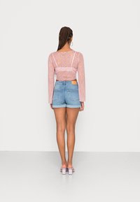 Vista trasera de una persona que lleva una blusa larga de manga con estampado floral en color rosa y shorts de mezclilla azul claros. La blusa tiene un borde de encaje; los shorts tienen una etiqueta en la parte trasera.