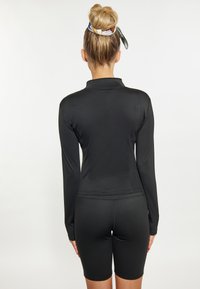 Maglietta sportiva nera a maniche lunghe con colletto alla coreana, abbinata a pantaloni ciclisti neri. Texture liscia, design aderente, senza motivi o accenti visibili.
