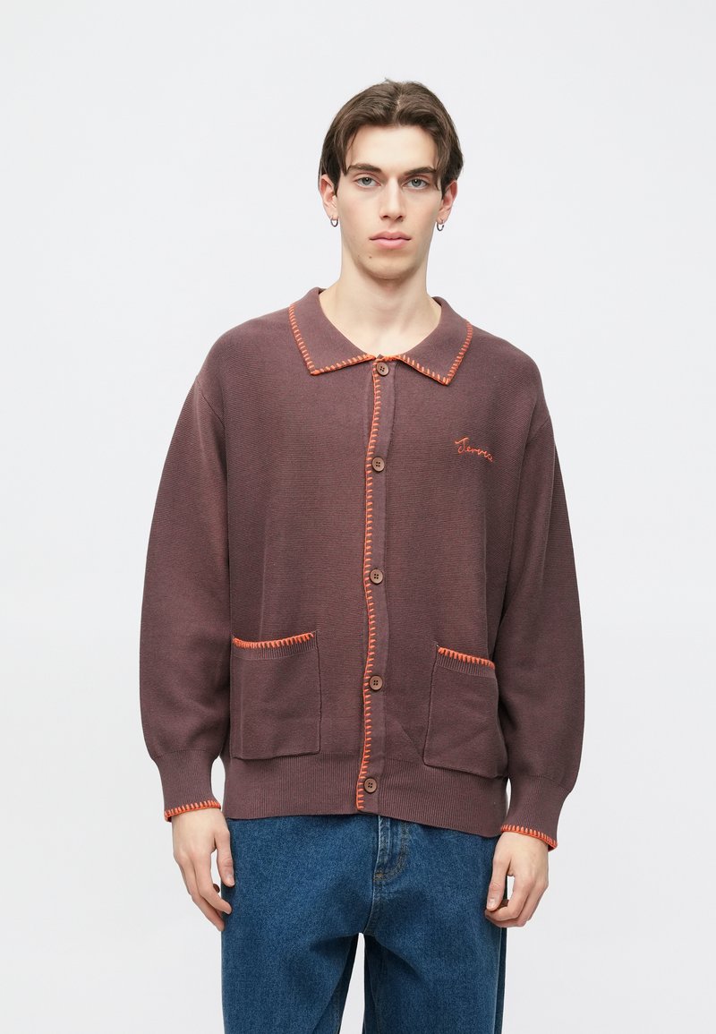 Hnedý kardigán s oranžovým prešitým golierom, zapínaním na gombíky a vreckami. Vyzdobený textúrovaným vzorom a minimálnym vyšívaným detailom.