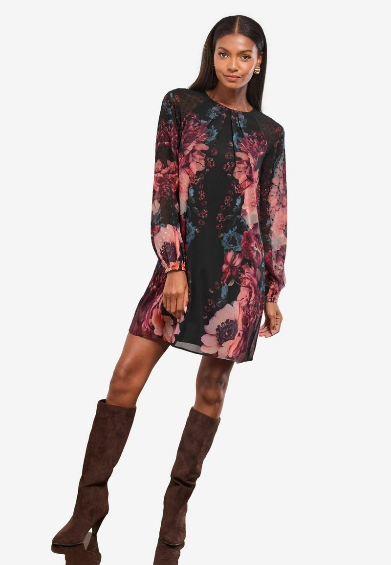 Rochie florală cu mâneci lungi, bază neagră, modele vibrante în nuanțe de roz și albastru. Stilizată cu cizme de piele din suede, până la genunchi, de culoare marron.