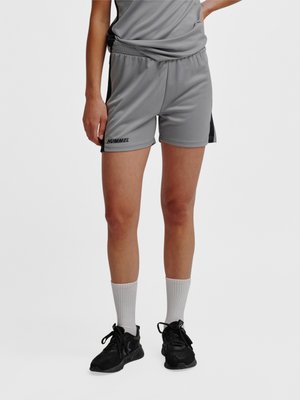 Personne portant un short de sport gris avec des bandes latérales noires, un t-shirt gris assorti, des chaussettes blanches et des chaussures de course noires.