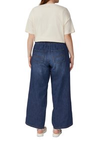 Szerokie niebieskie dżinsowe spodnie z elastycznym pasem i dwiema tylnymi kieszeniami, zestawione z kremowym t-shirtem z krótkim rękawem.