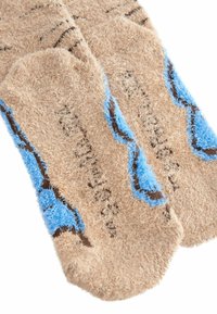 Tan fuzzy sokken met blauwe en bruine accenten; heeft een gestructureerd oppervlak en een patroon dat doet denken aan krullende lijnen.