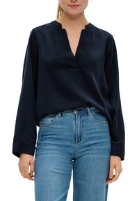 Navyblauwe blouse met lange mouwen en een V-hals, met een relaxte pasvorm, gemaakt van een gladde stof. Draagt met lichtblauwe slimfit jeans.