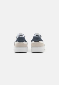 Weiße und marineblaue Sneaker mit einem oberen Teil aus glattem Leder und Wildleder, strukturierten Akzenten und einer gepolsterten Sohle mit geprägtem Branding.