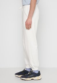 Witte katoenen sweatpants met elastische tailleband en boorden, met een relaxte pasvorm. Gekoppeld aan marineblauwe sneakers en lichtblauwe sokken.
