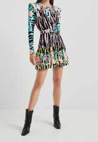 Robe longue à manches longues colorée avec des motifs zèbre et floraux, un corsage ajusté, un ourlet à volants et une ceinture assortie. Des bottines noires complètent le look.