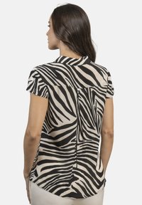 Blusa de manga corta con estampado de cebra en blanco y negro, hecha de una tela ligera, con dobladillo curvado y detalle de botón en la parte posterior.