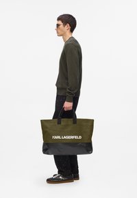 Borsa a spalla verde oliva con fondo nero, caratterizzata da manici doppi e un prominente logo bianco "KARL LAGERFELD". Realizzata in resistente materiale di tela.