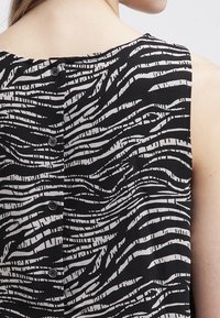 Top senza maniche bianco e nero con un motivo a strisce ondulate e piccoli bottoni sul retro, che mette in mostra una morbida trama del tessuto.
