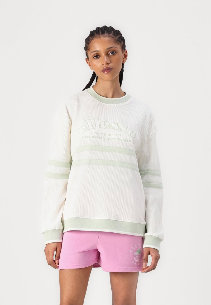 Maglione a coste color crema con strisce verde chiaro, con logo ricamato. Abbinato a pantaloni corti rosa con una piccola stampa del logo.