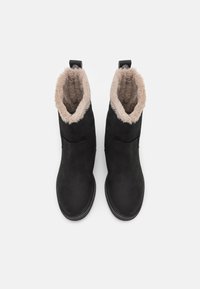Botas negras de tobillo con un suave forro de piel sintética beige en la parte superior, exterior de textura lisa y diseño de punta redondeada. Suela de goma plana.