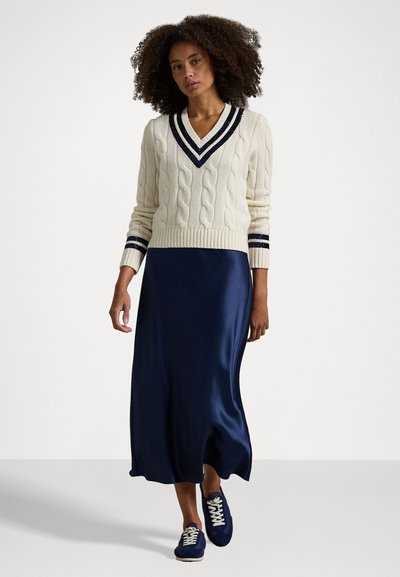 Pull en maille torsadée crème avec un col en V marine et des accents rayés, associé à une robe maxi en satin lisse marine et des baskets marines.