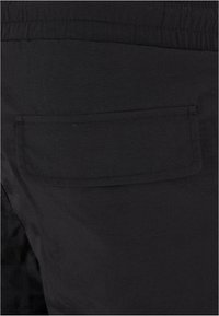 Black shorts with a textured fabric, featuring a rear patch pocket and an elastic waistband, emphasizing functionality and simple design.