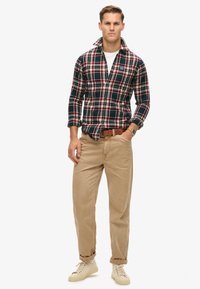 Geruit flanellen shirt in marineblauw, rood en groen; beige katoenen broek; crèmekleurige sneakers; button-down kraag; relaxed fit.