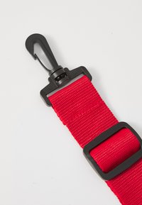 Correa de nailon roja con un clip de plástico negro, con una superficie texturizada y una hebilla rectangular negra para el ajuste.