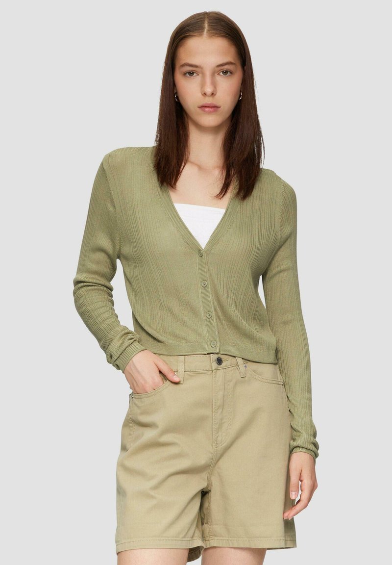 Hellgrüner gerippter Cardigan mit tiefem V-Ausschnitt, Knopfverschluss und langenÄrmeln, kombiniert mit beigen Shorts. Glatte Textur, lässiges Design.