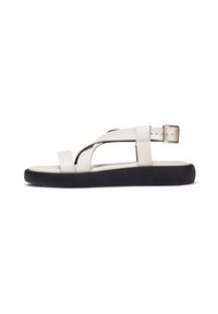 Sandal de cuero en tonos crema claros con correas cruzadas, hebilla ajustable en el tobillo y suela de goma negra. Diseño sencillo y plano con minimalismo en los detalles.