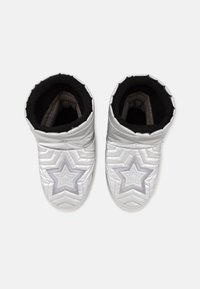 Par de zapatillas blancas acolchadas con diseños de estrellas plateadas en la parte superior y forro interior negro, vista desde arriba sobre un fondo neutro.