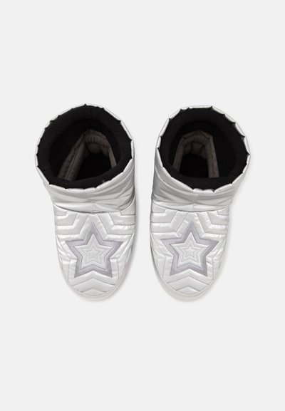 Paire de chaussons blancs rembourrés avec des motifs d'étoiles argentées sur le dessus et une doublure intérieure noire, vue de dessus sur un fond neutre.
