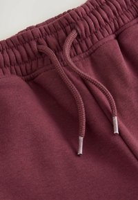 Bordeaux sweatpants med elastisk talje og snøre, glat tekstur og forstærkede syninger ved kanten og lommerne.