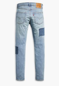 Jean en denim bleu clair avec une texture délavée, comportant deux accents en patch et une étiquette sur la ceinture. Design classique à cinq poches.