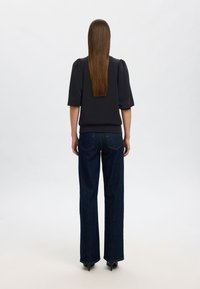 Melns īsām piedurknēm krekls ar pūkainām plecu daļām, apvienots ar augsto jostasvietu tumši ziliem džinsiem un melniem papēžu kurpēm. Gluda tekstūra, pieguļoša siluets.