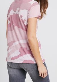 Růžové kamuflážové tričko s krátkým rukávem, vyrobené z měkké tkaniny, s nepravidelnými vzory v různých odstínech růžové a světle šedé.