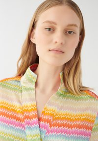 Flerfärgad blus med zigzag-mönster i lätt och genomskinligt tyg. Har krage och en variation av pastellfärger inklusive rosa, grönt och orange.