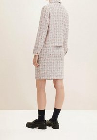 Ensemble jupe et veste en tweed avec un motif texturé multicolore. Des chaussures à plateforme noires et des chaussettes bleu marine complètent la tenue.