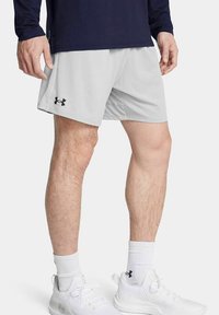 Shorts de sport gris clair avec une taille élastique et des poches latérales, arborant un logo noir sur la jambe gauche. Portés avec des baskets blanches.