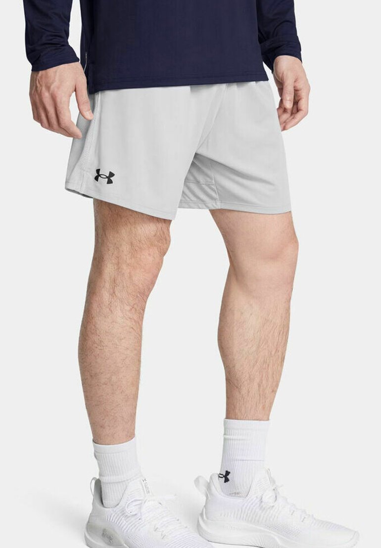 Shorts de sport gris clair avec une taille élastique et des poches latérales, arborant un logo noir sur la jambe gauche. Portés avec des baskets blanches.