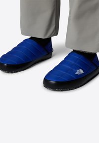Pantofole blu imbottite con suole in gomma nera, caratterizzate da un design trapuntato e un logo bianco. Parte superiore testurizzata e vestibilità ammortizzante per il comfort.